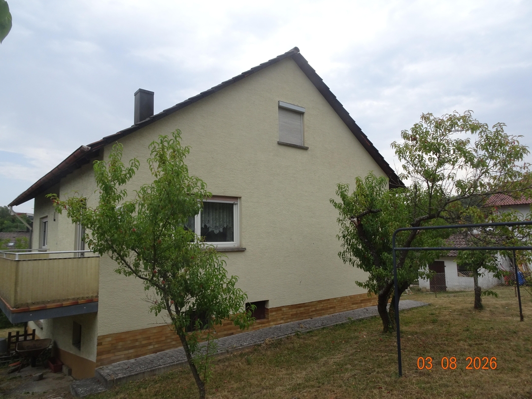 Außenansicht des Gebäudes es ist ein Haus zu sehen. Vor dem Haus ist eine Wiese mit Bäumen.